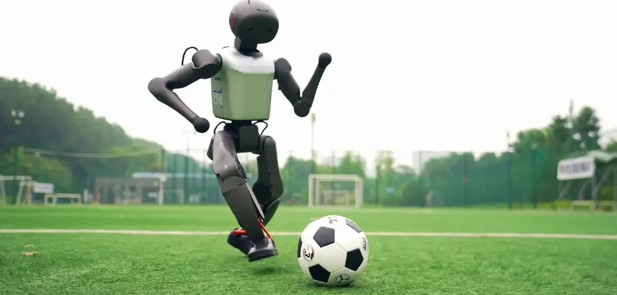 A humanoid robot striking a football on a grass pitch